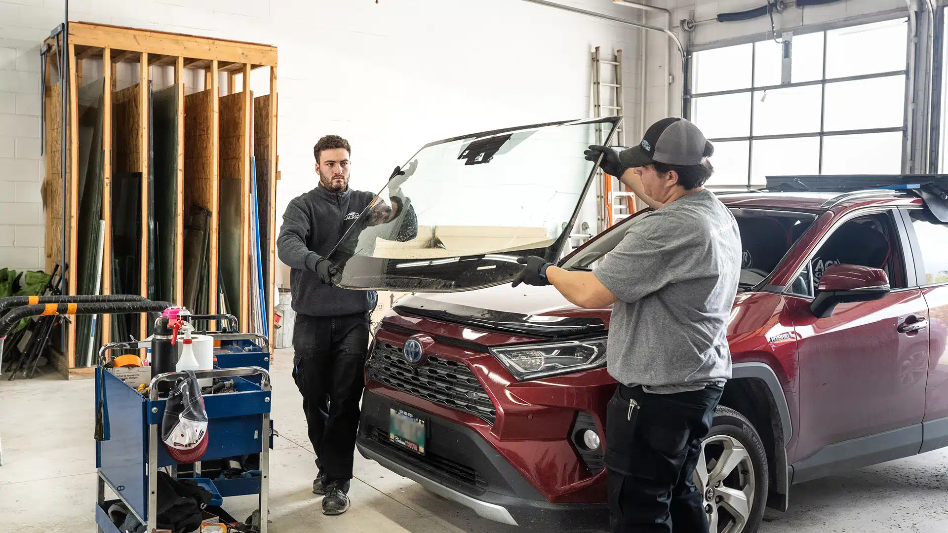 Two male auto mechanics holding a windshield to replace in a vehicle